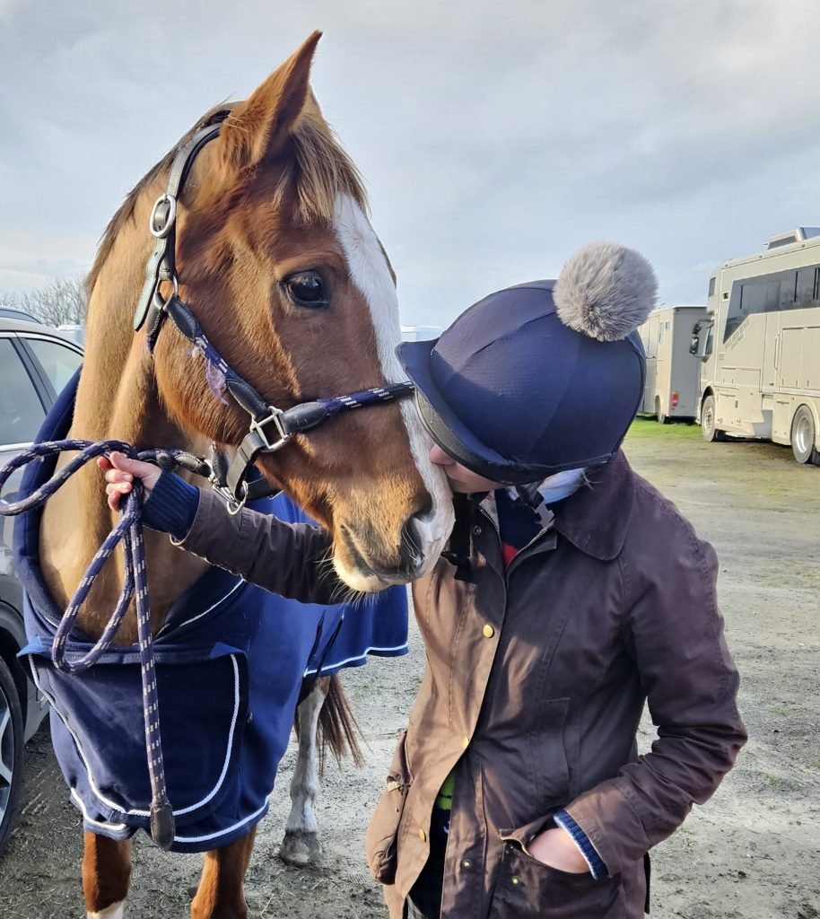 Image of a woman in horse riding clothes and hat next to a horse